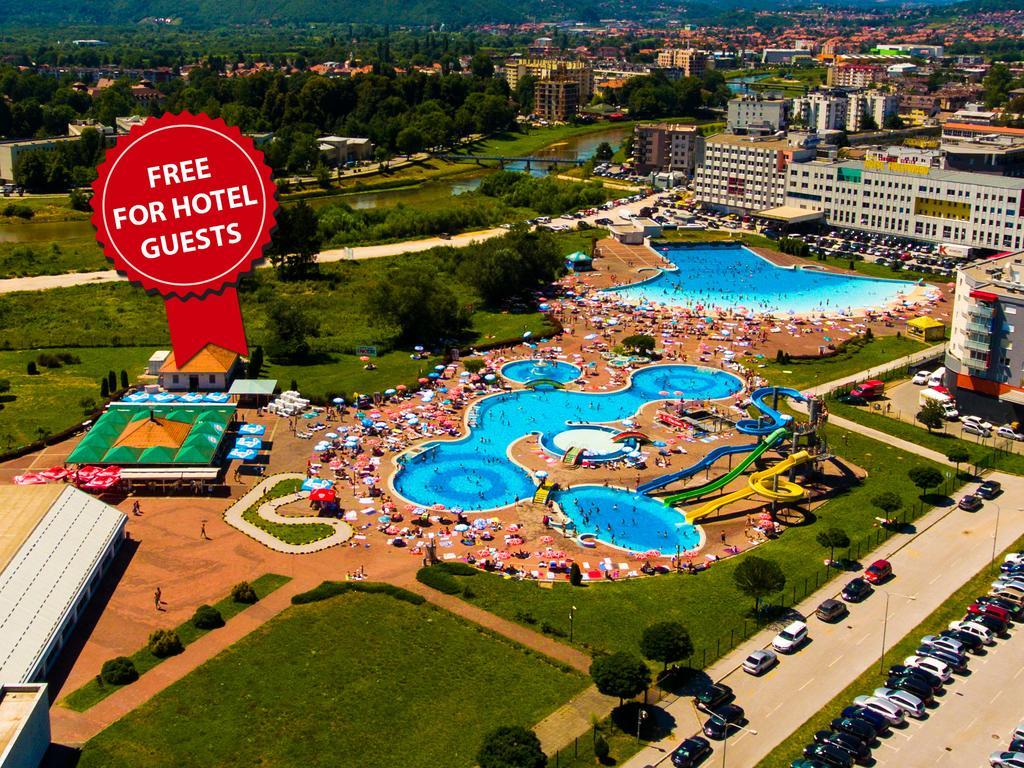 Hotel Hills Sarajevo Congress & Thermal Spa Resort Ilidža Luaran gambar The photo shows an aerial view of a large swimming pool area, likely part of a hotel or resort. There are several pools of different shapes and sizes, including one that resembles a Mickey Mouse shape. The area is filled with numerous sun loungers an